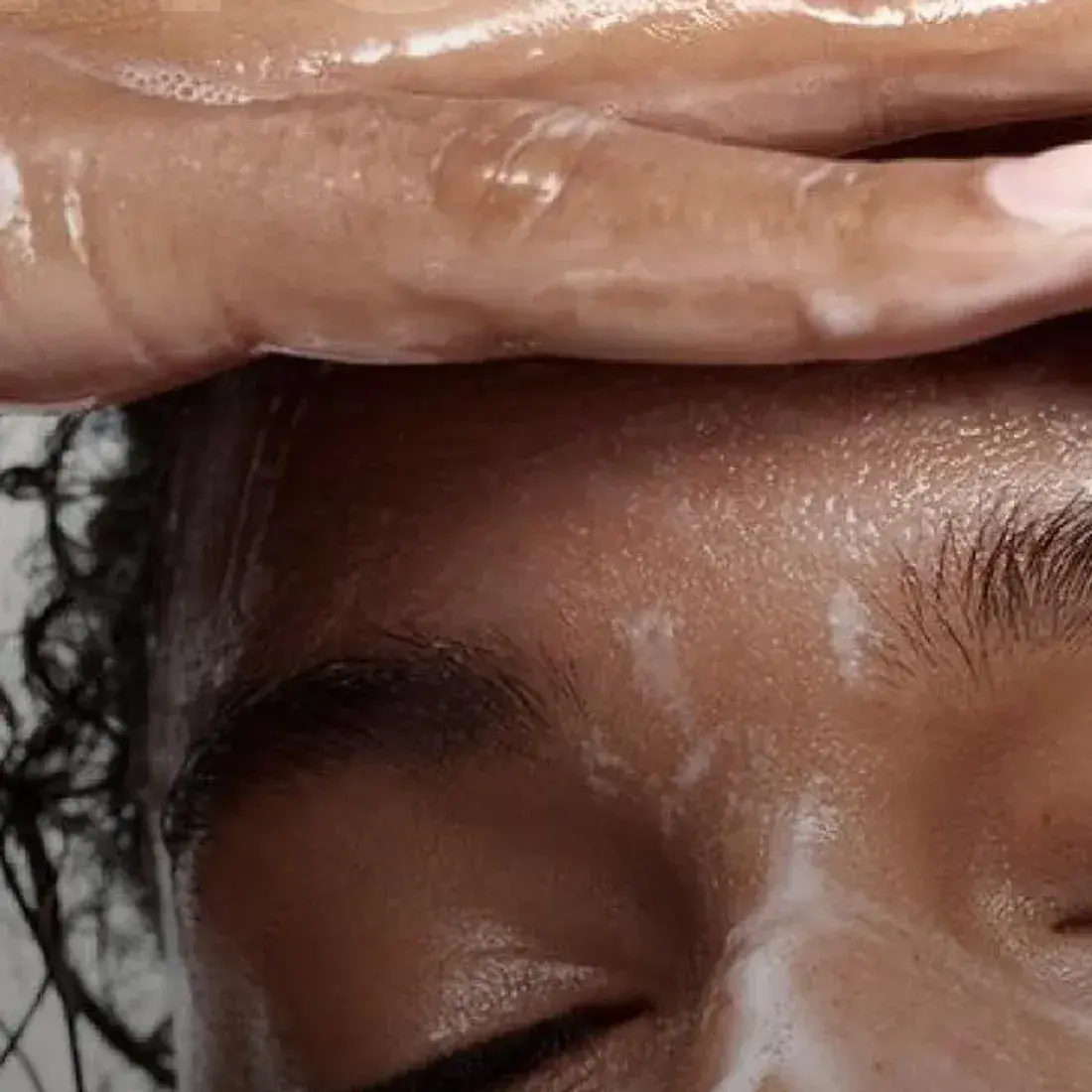 Mãos deslizando sobre a testa em movimento de massagem facial, pele com produto