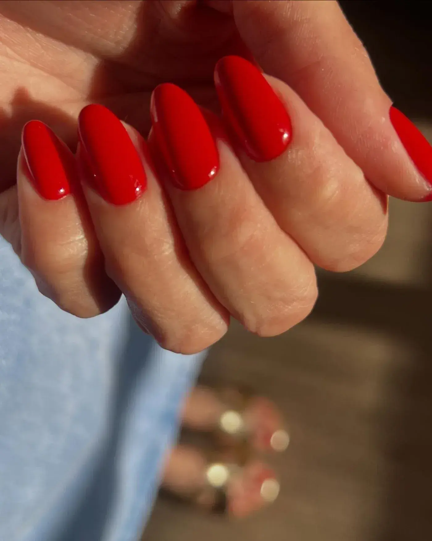 Mão fechada em close com unhas em formato amêndoa esmaltadas em vermelho brilhante