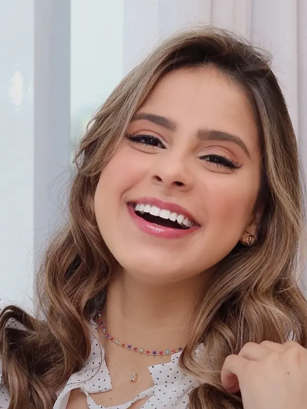 Alana Leandro rindo em retrato aproximado, com a luz de uma janela ao fundo