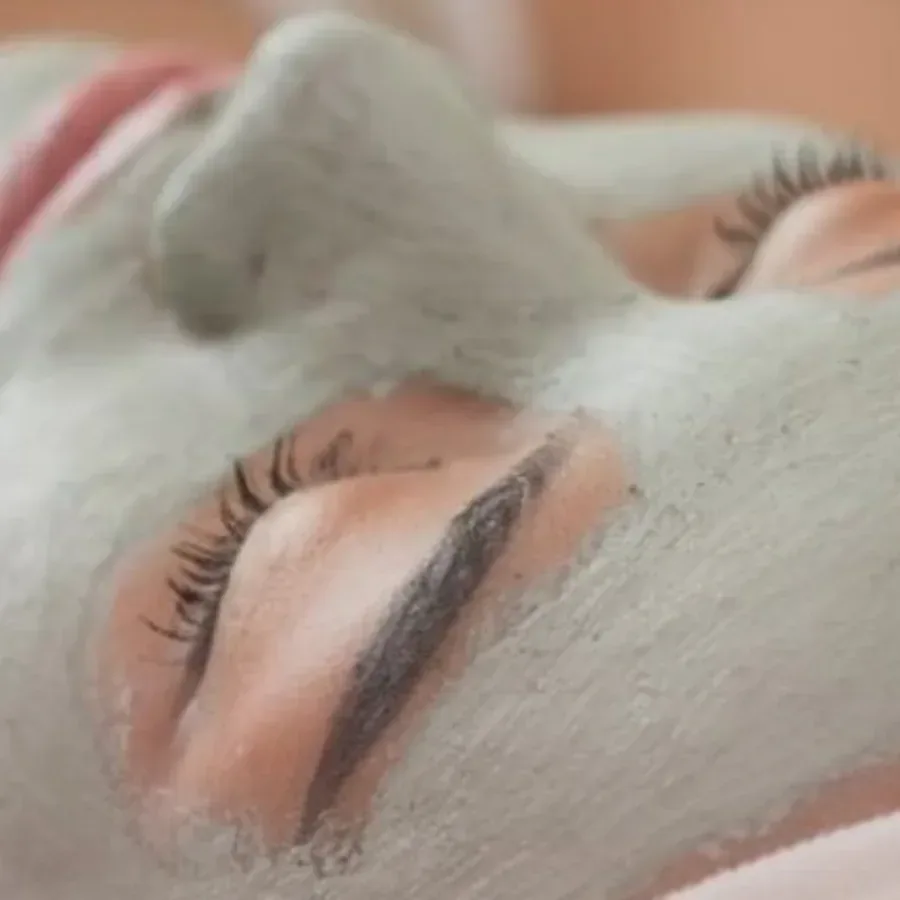 Rosto de olhos fechados recebendo máscara de argila aplicada com pincel chanfrado