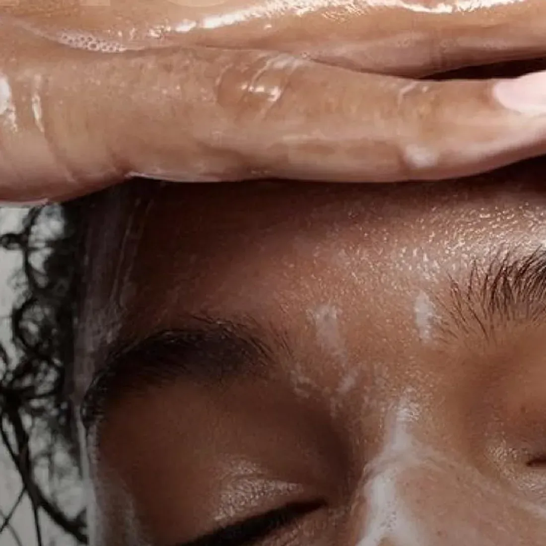 Mãos deslizando sobre a testa em movimento de massagem facial, pele com produto