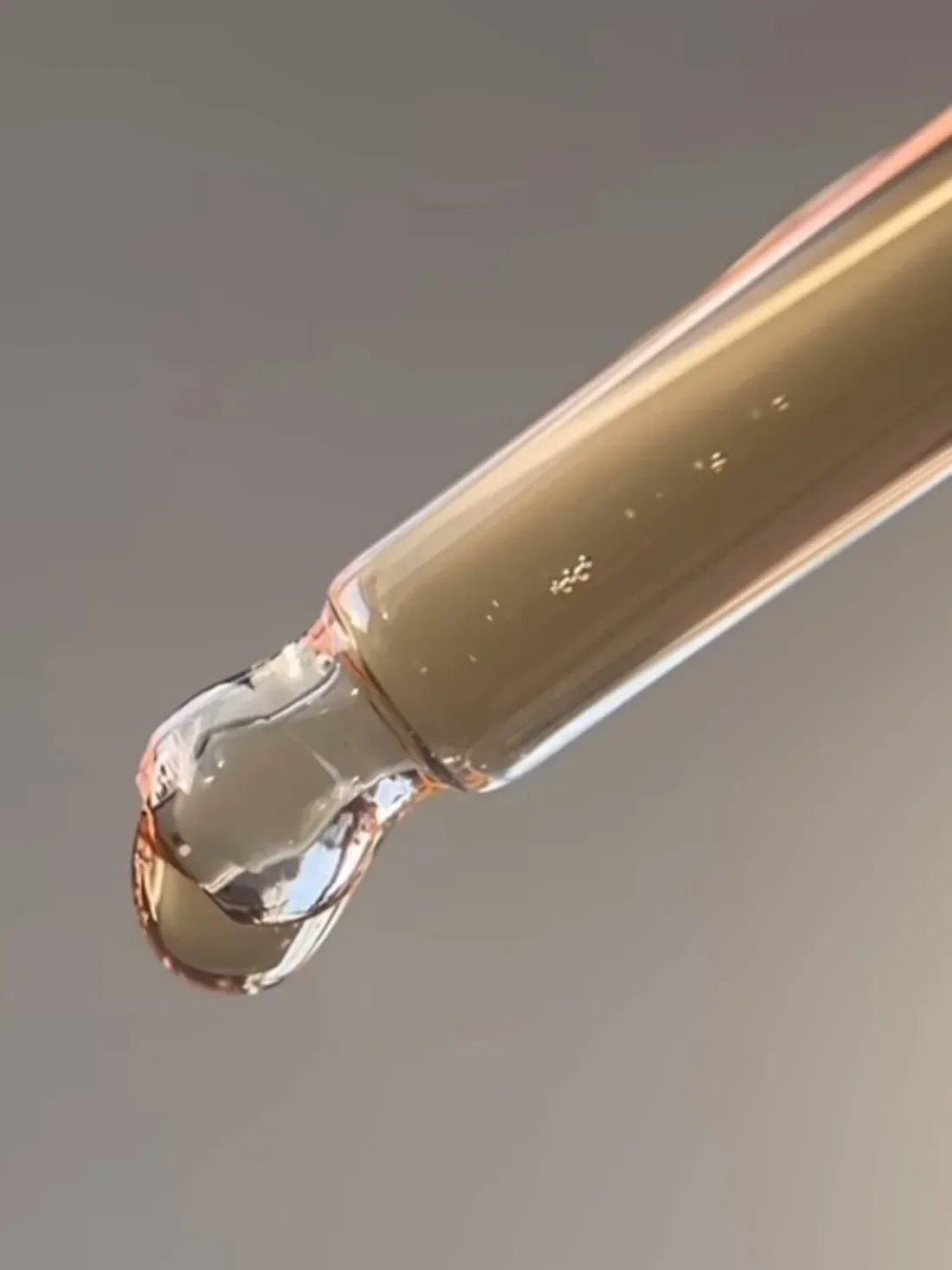 Conta-gotas de vidro com uma gota de ativo dourado prestes a cair, sobre fundo claro