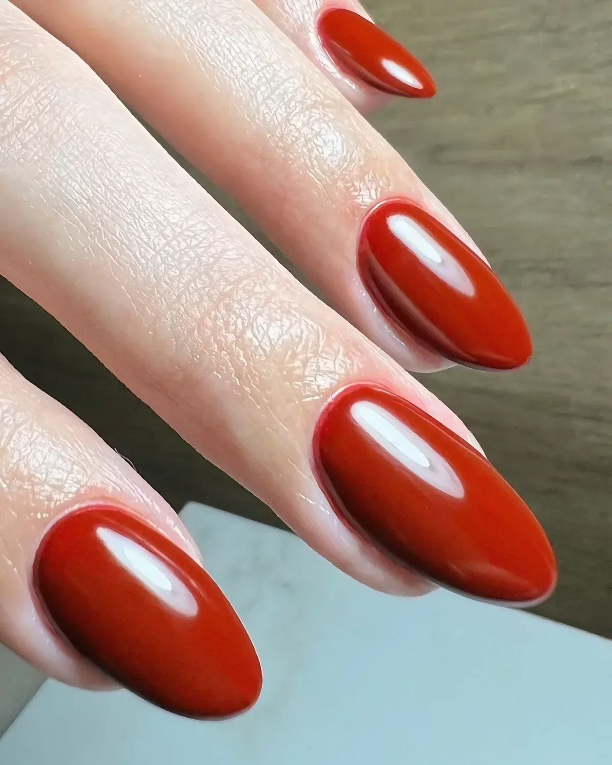 Unhas em formato amêndoa esmaltadas em vermelho terracota, com acabamento espelhado