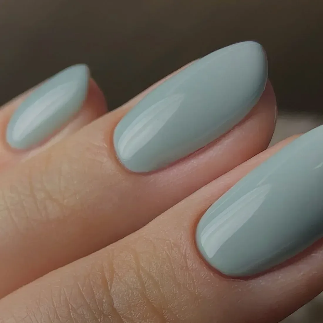 Unhas longas esmaltadas em verde sálvia claro, em close sobre fundo neutro